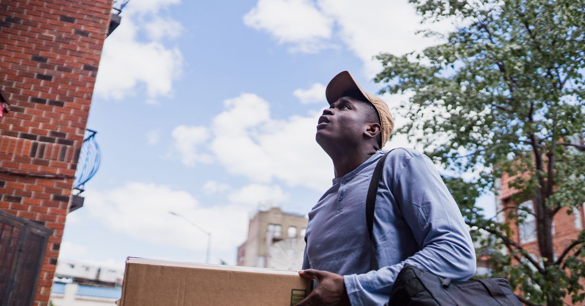 Man delivering a package in a city neighborhood, looking up at the building.